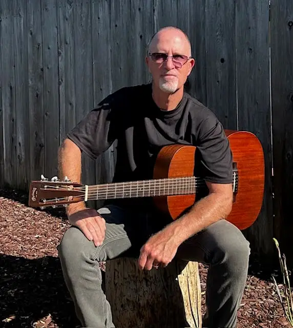 Mark Torpey seated with an acoustic guitar.